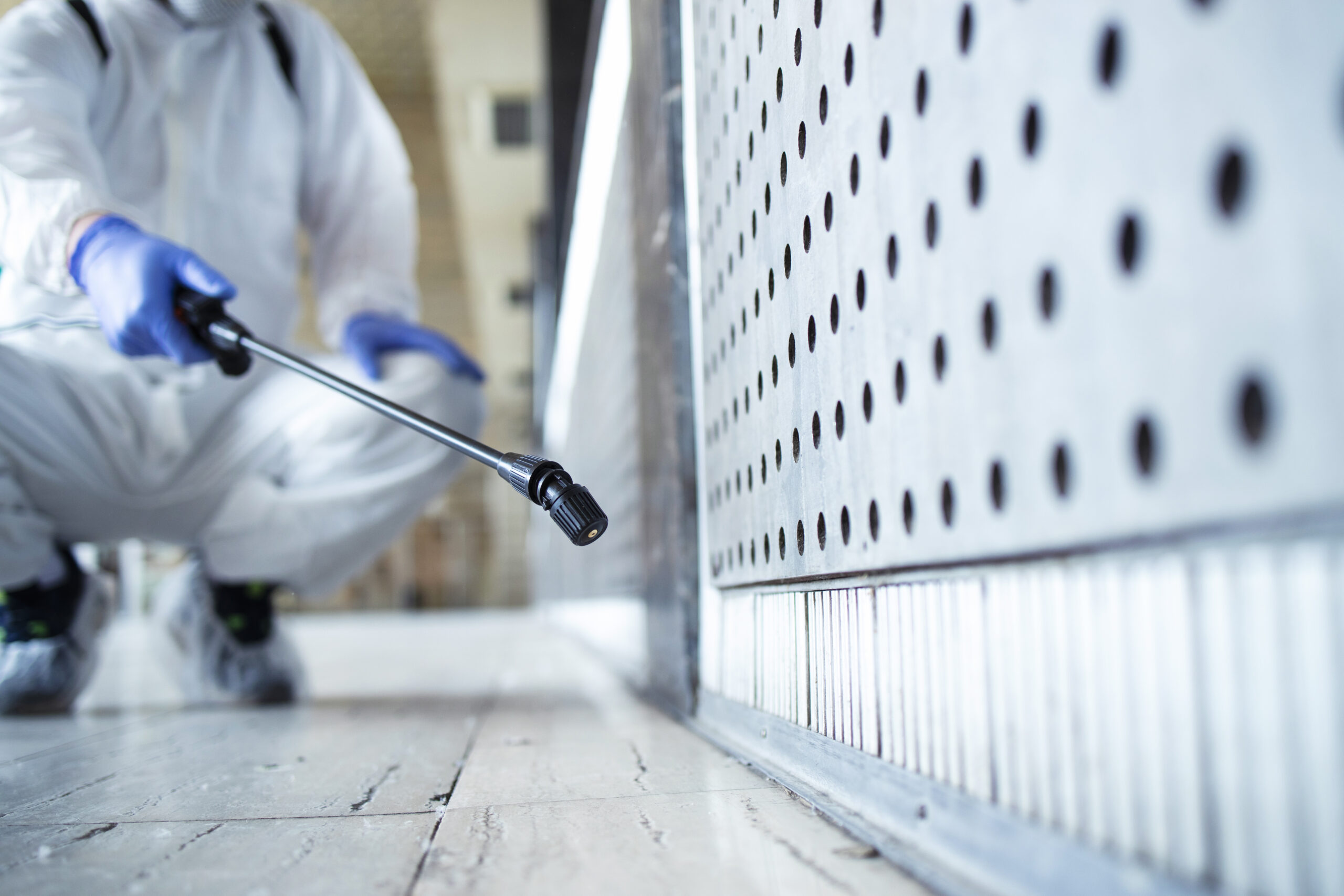 Person in white chemical protection suit disinfecting surfaces to prevent mold and contamination in public areas.