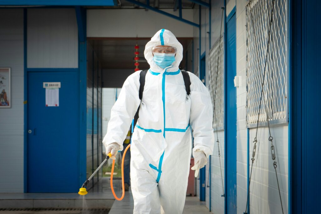 Professional in protective gear using a sprayer for mold remediation outside a residential property, emphasizing expertise in safe and effective mold removal techniques.